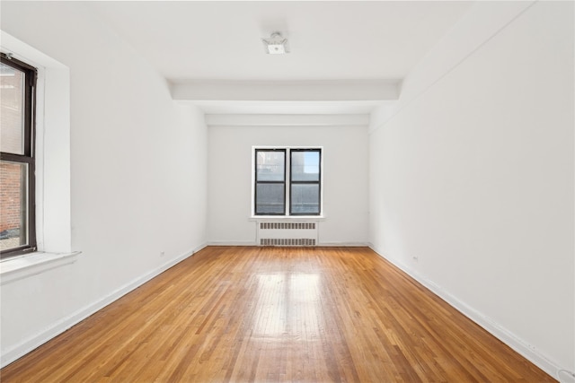 unfurnished room with light hardwood / wood-style floors, radiator heating unit, and beam ceiling