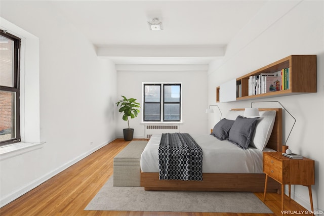 bedroom with radiator, hardwood / wood-style floors, and beam ceiling