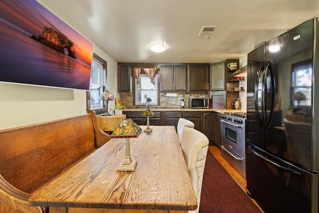 kitchen with dark brown cabinets, stainless steel appliances, tasteful backsplash, and wall chimney range hood