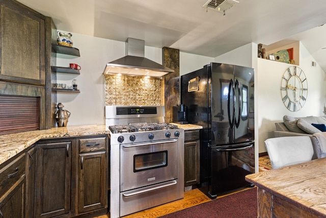 kitchen featuring black refrigerator, dark brown cabinets, stainless steel range with gas cooktop, and wall chimney exhaust hood