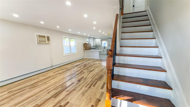 stairs with a wall unit AC, a baseboard heating unit, and hardwood / wood-style flooring