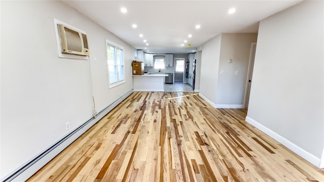 kitchen with a wall unit AC, white cabinetry, light hardwood / wood-style floors, and baseboard heating