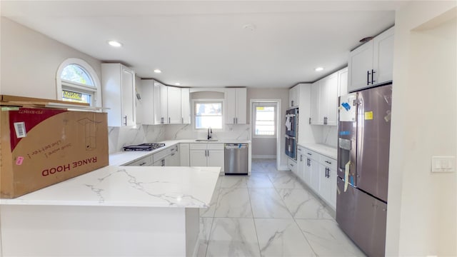 kitchen with sink, white cabinetry, light stone counters, kitchen peninsula, and stainless steel appliances