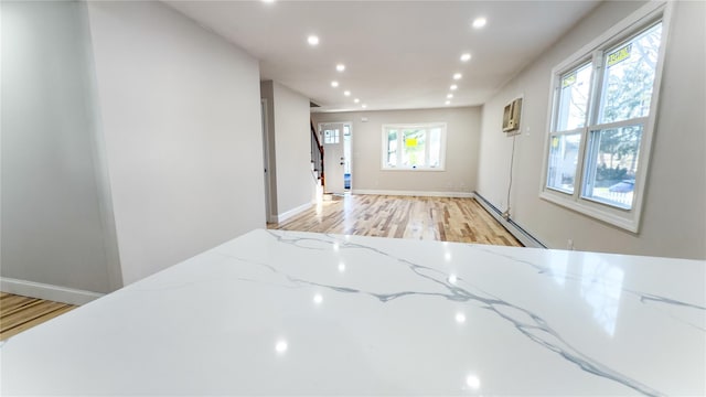 kitchen with a wall mounted AC, light stone counters, light hardwood / wood-style flooring, and a baseboard heating unit