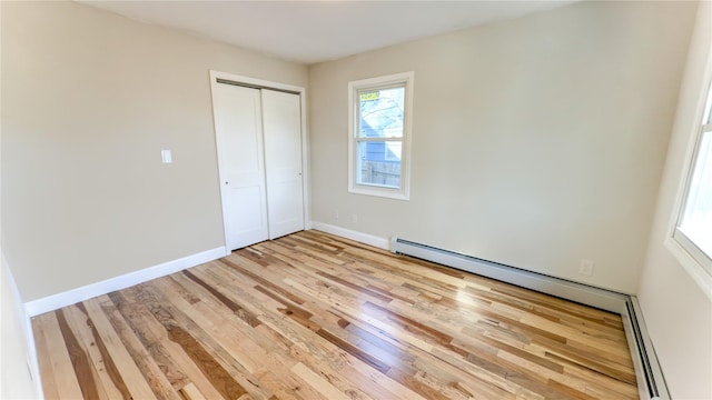 unfurnished bedroom featuring light hardwood / wood-style flooring, a closet, and a baseboard heating unit