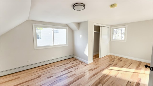 unfurnished bedroom featuring a closet, light wood-type flooring, lofted ceiling, and a baseboard heating unit