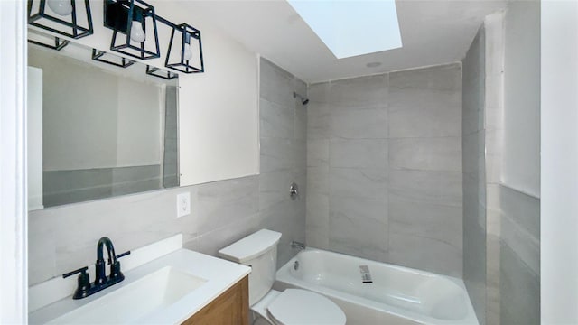 full bathroom featuring a skylight, vanity, tile walls, toilet, and tiled shower / bath