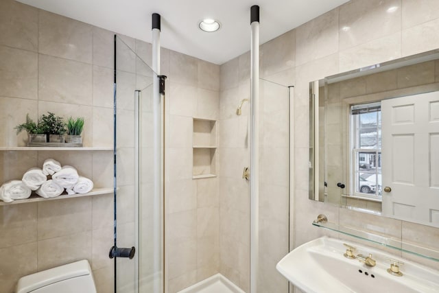 bathroom featuring toilet, tasteful backsplash, walk in shower, tile walls, and sink