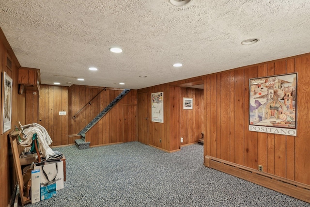 basement featuring wood walls, a textured ceiling, carpet flooring, and a baseboard heating unit