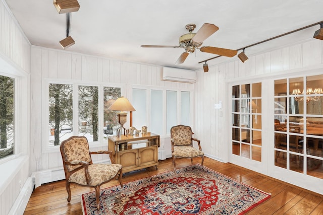 sunroom / solarium featuring ceiling fan with notable chandelier, an AC wall unit, rail lighting, and baseboard heating