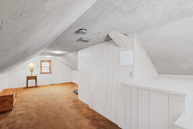 bonus room featuring vaulted ceiling, wood walls, light colored carpet, and a textured ceiling