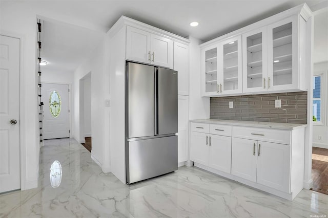 kitchen with tasteful backsplash, stainless steel fridge, white cabinets, and light stone countertops