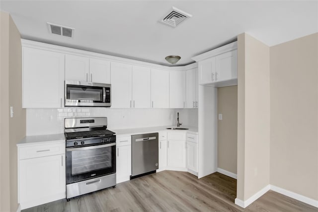 kitchen with sink, light wood-type flooring, appliances with stainless steel finishes, decorative backsplash, and white cabinets