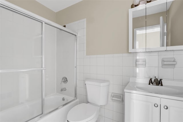 full bathroom with vanity, combined bath / shower with glass door, tile walls, and toilet