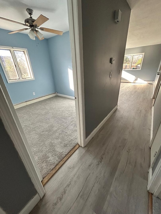 corridor with hardwood / wood-style floors, a baseboard heating unit, and a healthy amount of sunlight