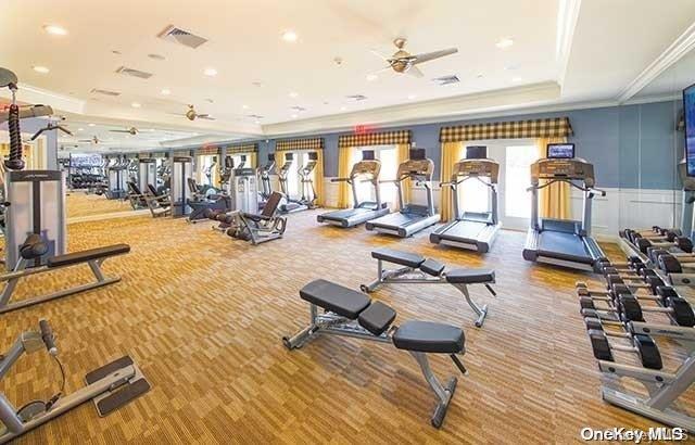 workout area featuring a tray ceiling, ceiling fan, crown molding, and carpet floors