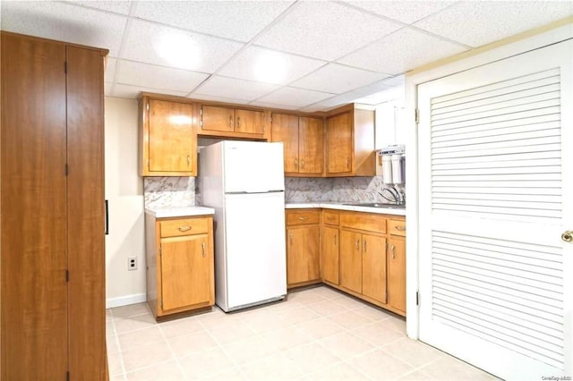 kitchen featuring a paneled ceiling, decorative backsplash, sink, and white fridge