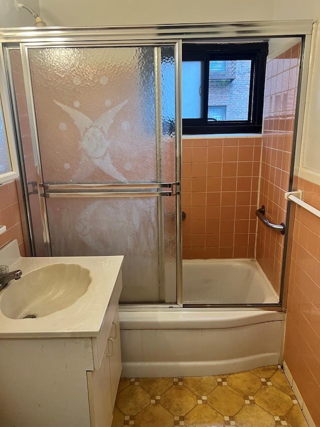 bathroom featuring shower / bath combination with glass door, vanity, plenty of natural light, and tile walls