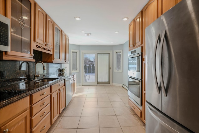 kitchen featuring sink, stainless steel appliances, dark stone countertops, decorative backsplash, and light tile patterned flooring