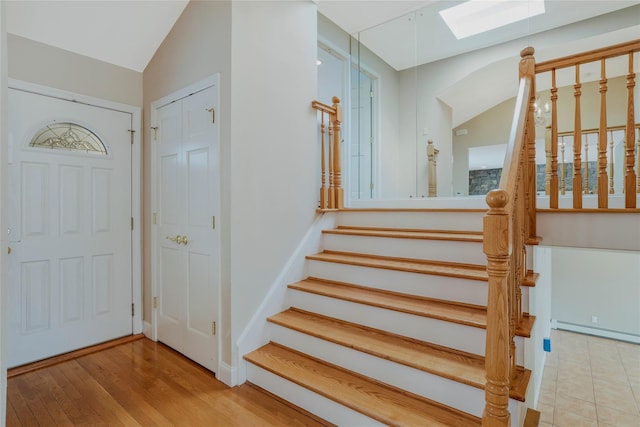 entrance foyer with light hardwood / wood-style flooring, baseboard heating, and vaulted ceiling with skylight