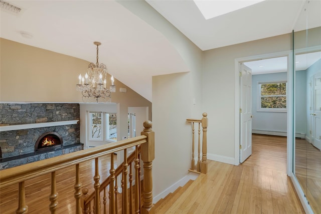 hallway with vaulted ceiling, light hardwood / wood-style floors, a baseboard radiator, and a notable chandelier