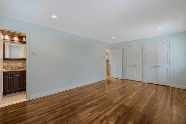 unfurnished bedroom with two closets, light wood-type flooring, and ensuite bath