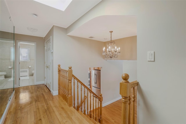 corridor featuring radiator heating unit, a skylight, light hardwood / wood-style flooring, and an inviting chandelier