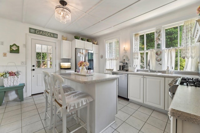 45 Shore Rd, East Setauket, NY 11733 - kitchen featuring stainless steel appliances, light tile patterned floors, white cabinetry, a chandelier, and a kitchen island