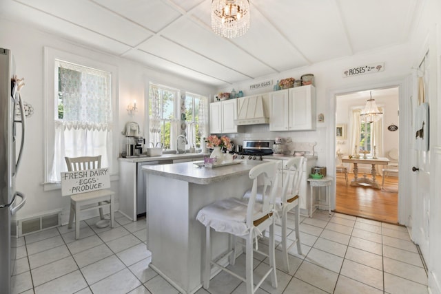 kitchen featuring a center island, stainless steel appliances, light tile patterned floors, premium range hood, and white cabinets