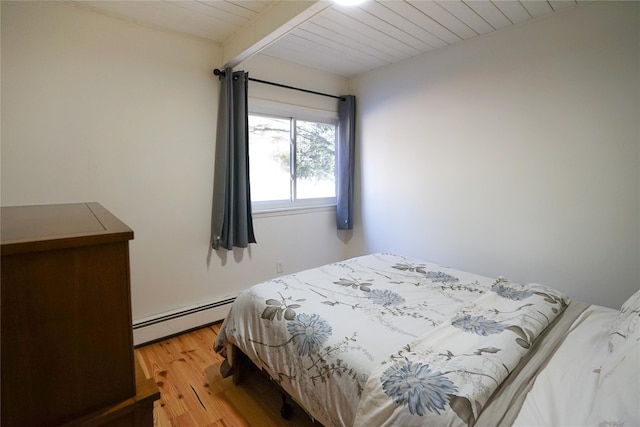 bedroom with beam ceiling, light wood-type flooring, and baseboard heating