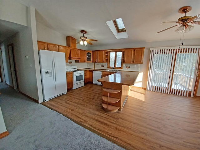 kitchen with white appliances, vaulted ceiling with skylight, light hardwood / wood-style floors, and sink