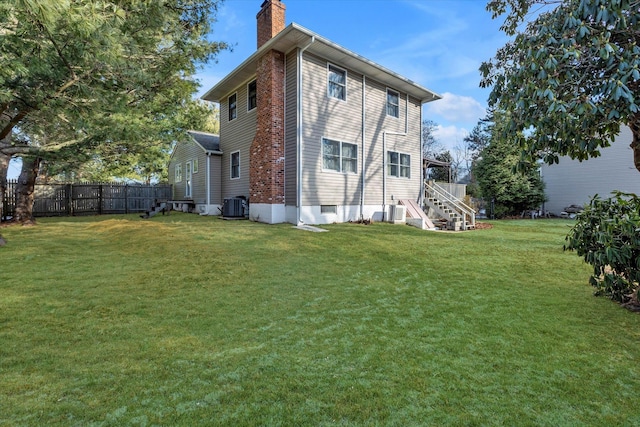 back of house featuring central air condition unit, a chimney, a yard, and fence