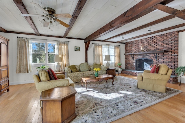 living room with beam ceiling, light hardwood / wood-style floors, a brick fireplace, and ceiling fan