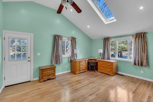 office space featuring light wood-type flooring, high vaulted ceiling, a ceiling fan, a skylight, and baseboards