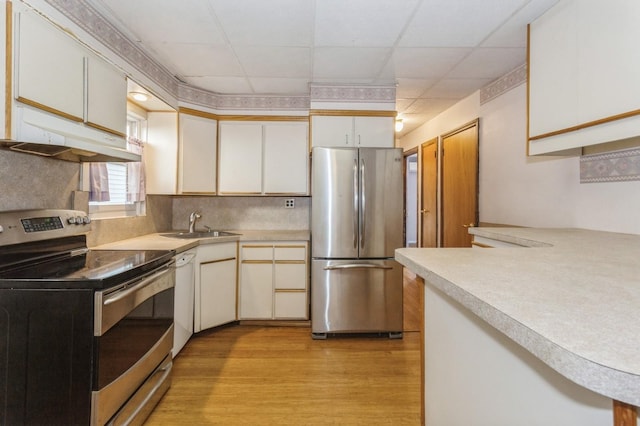 kitchen with a paneled ceiling, white cabinets, light wood-type flooring, and appliances with stainless steel finishes