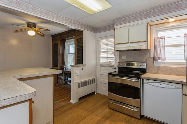 kitchen with dishwasher, a drop ceiling, radiator heating unit, light hardwood / wood-style flooring, and stainless steel electric range