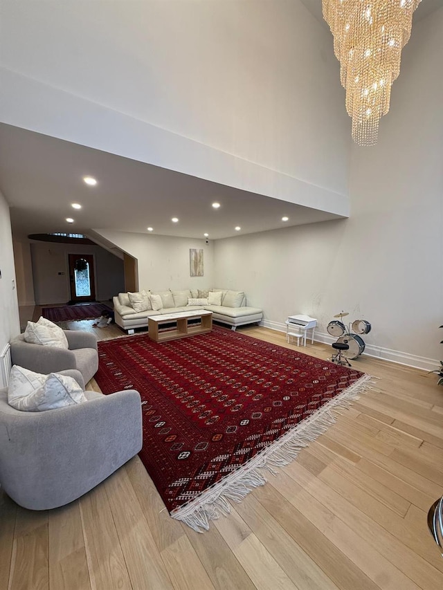 living area with baseboards, wood finished floors, an inviting chandelier, a high ceiling, and recessed lighting