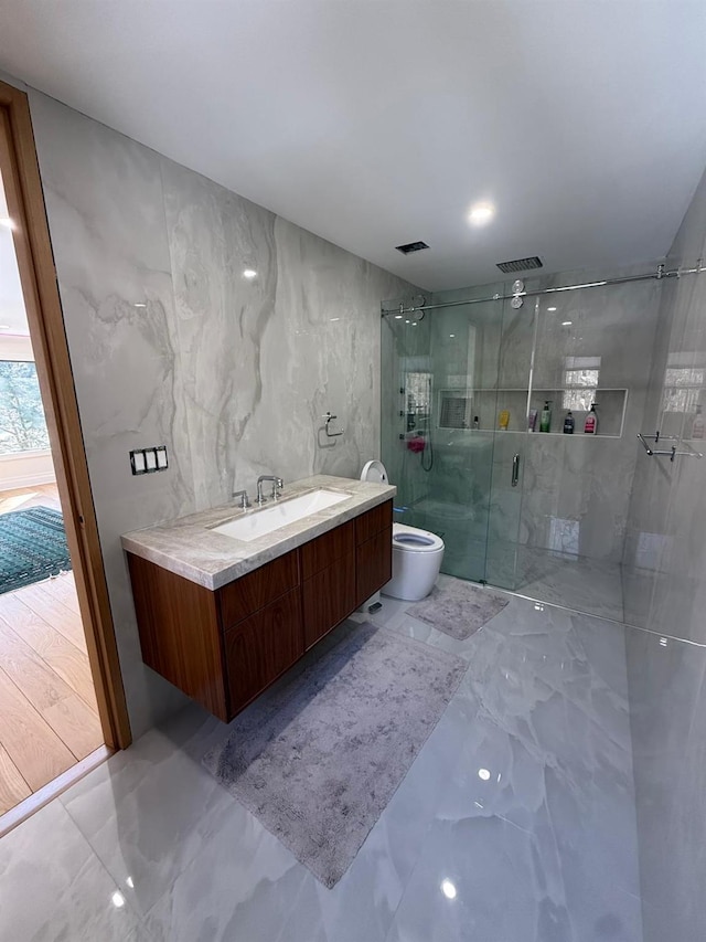 bathroom featuring toilet, vanity, tile walls, marble finish floor, and a stall shower