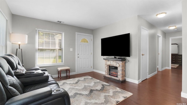 living room featuring dark hardwood / wood-style flooring, a stone fireplace, and a healthy amount of sunlight