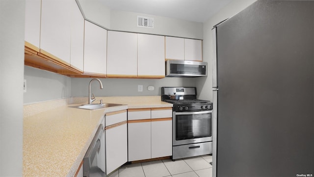 kitchen featuring sink, white cabinetry, stainless steel appliances, and light tile patterned floors