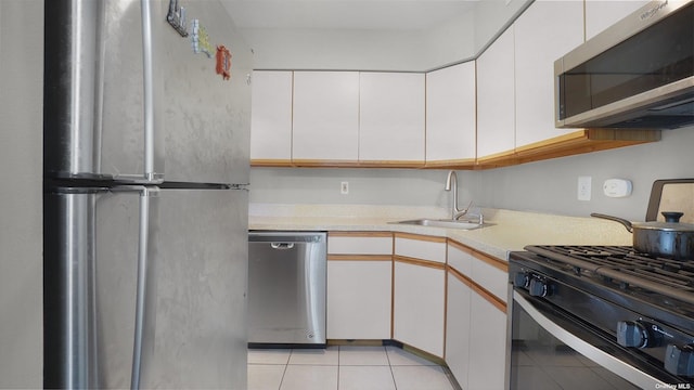 kitchen with light tile patterned floors, stainless steel appliances, white cabinetry, and sink