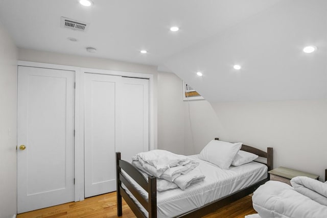 bedroom featuring multiple closets, wood-type flooring, and vaulted ceiling