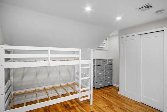 unfurnished bedroom featuring lofted ceiling, wood-type flooring, an AC wall unit, and a closet