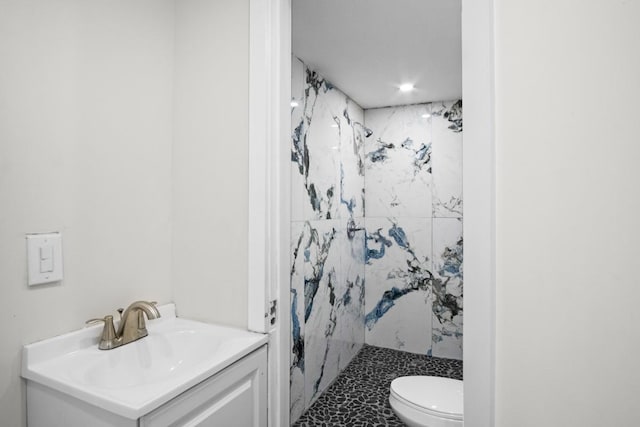 bathroom with a tile shower, vanity, and toilet