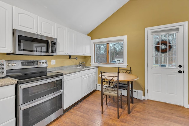 kitchen with appliances with stainless steel finishes, white cabinets, vaulted ceiling, and sink