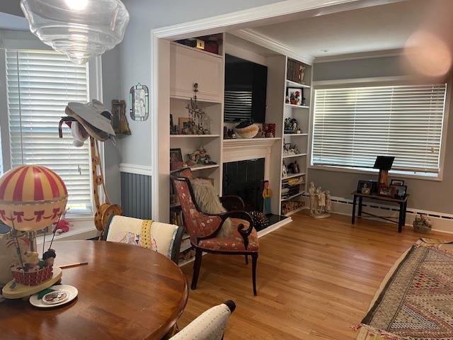 living area featuring crown molding, built in features, baseboard heating, and light hardwood / wood-style flooring