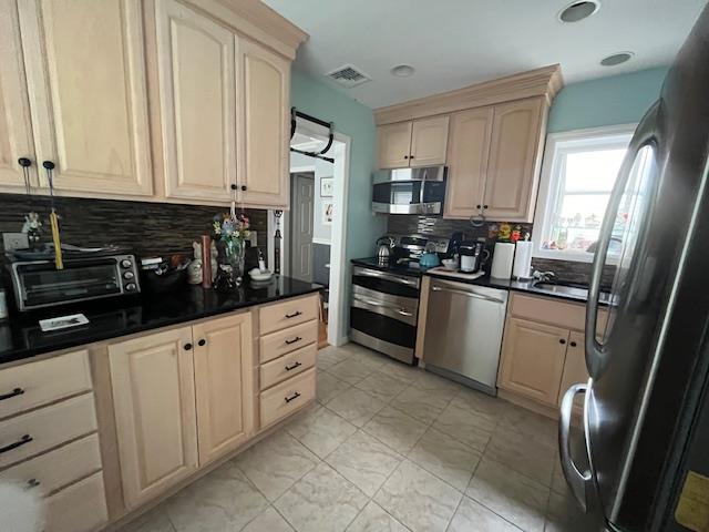 kitchen with tasteful backsplash, light brown cabinetry, and appliances with stainless steel finishes