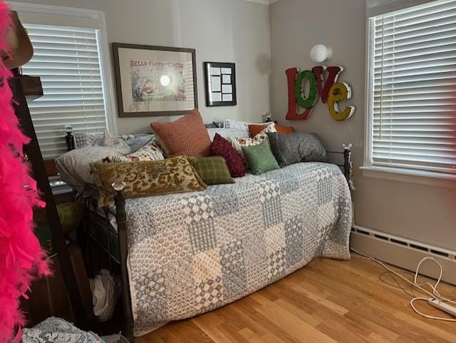 bedroom with hardwood / wood-style floors, a baseboard radiator, and multiple windows