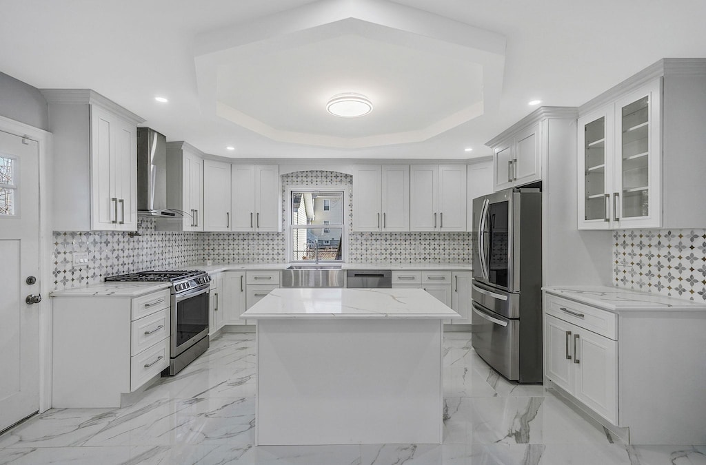 kitchen with white cabinets, a raised ceiling, wall chimney range hood, and stainless steel appliances