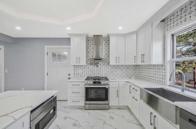 kitchen featuring white cabinets, appliances with stainless steel finishes, wall chimney exhaust hood, and sink